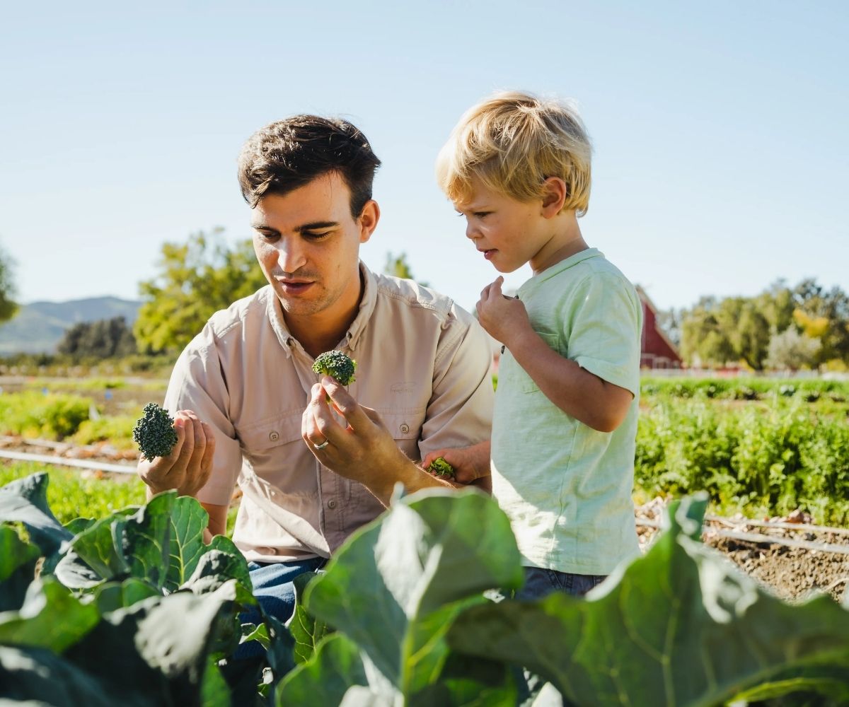 Adult and young child examining vegetables together in a garden.